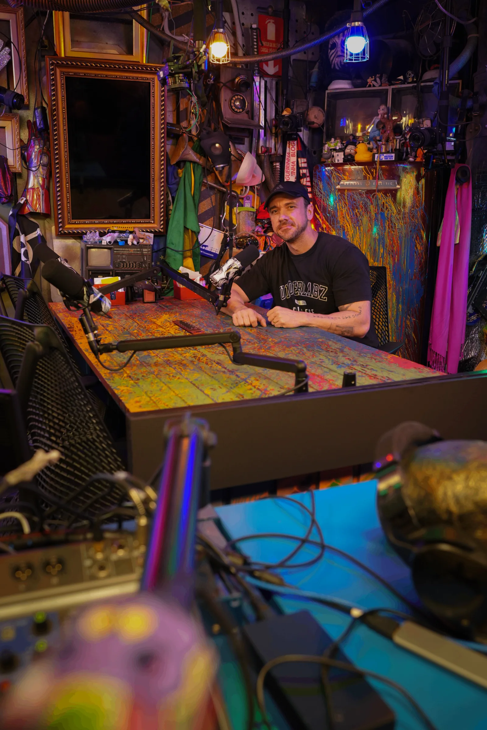 Will Jardim de boné sentado à mesa de um estúdio de podcast durante gravação